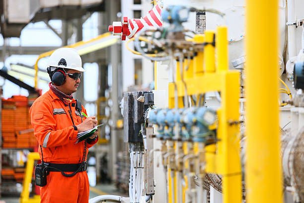 Technician in orange coveralls, white hard hat and ear defenders inspecting instruments